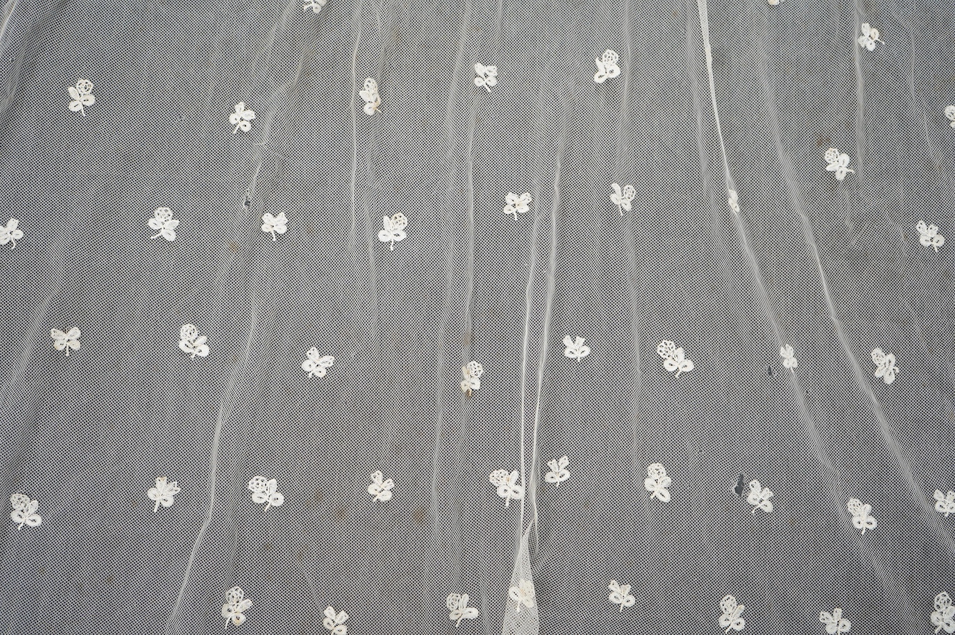 An Edwardian Brussels bobbin lace on net wedding veil, with all over bobbin lace appliqué spot motifs, within an ornate bobbin lace border, approximately 175cm x 168cm. Condition - there are various rust stains and holes